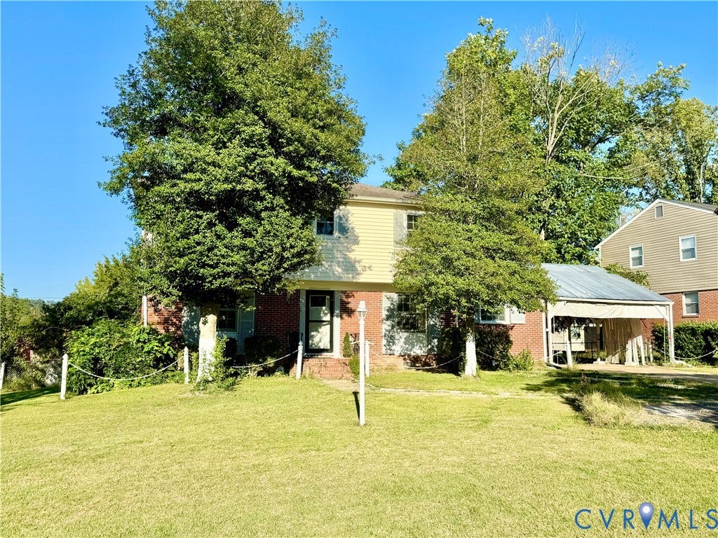 Two-story residence featuring a brick and siding exterior, established front yard with mature trees, and a covered carport with a metal roof