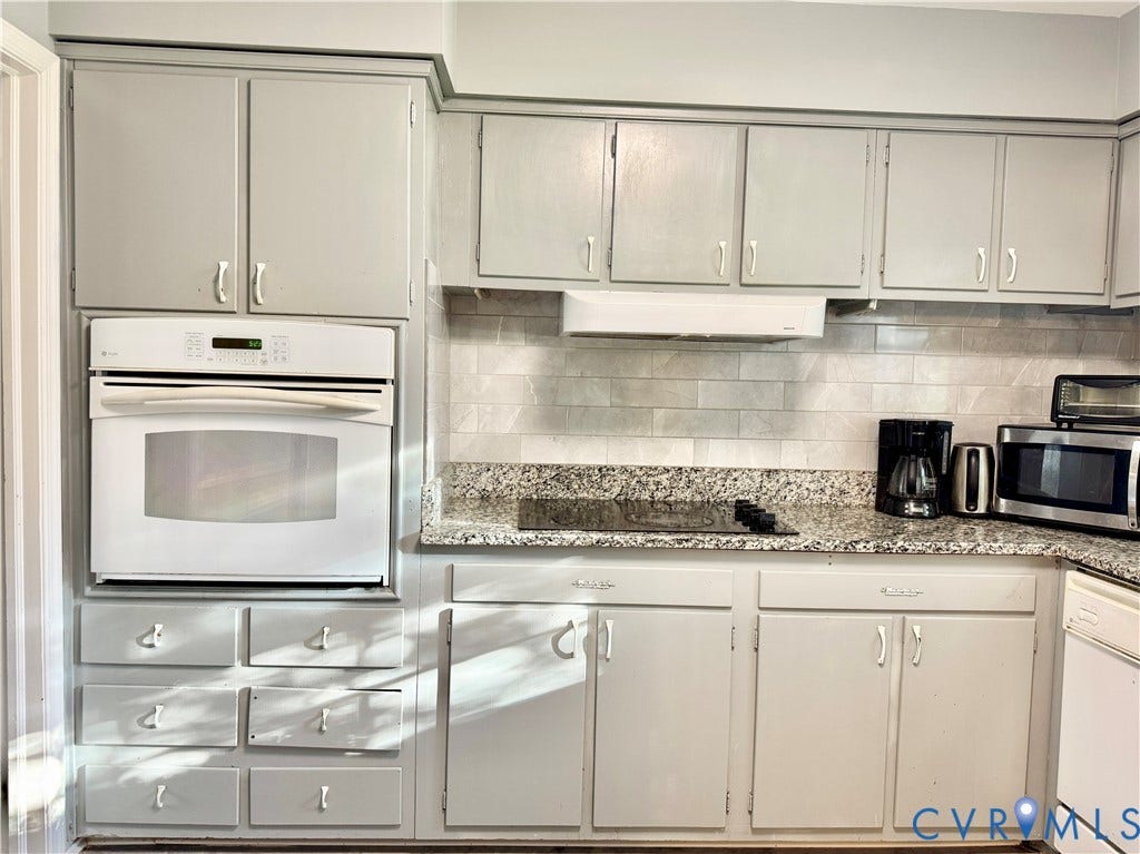 Built-in oven, integrated cooktop, stone-finish countertops, tiled backsplash, and light-toned cabinetry