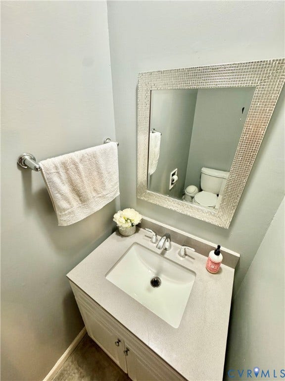 White vanity with brushed nickel hardware, integrated rectangular sink, gray countertop, and framed mirror
