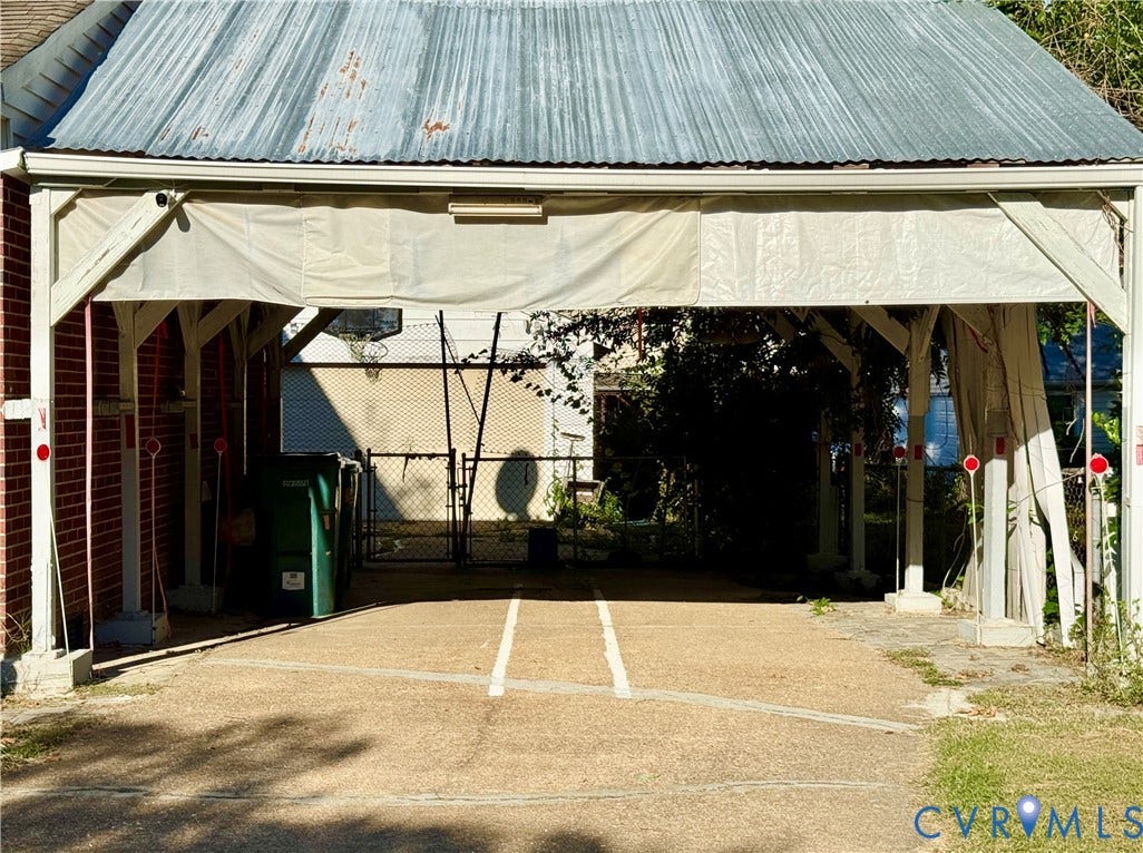 Covered carport with a corrugated metal roof, brick accent wall, and a concrete base
