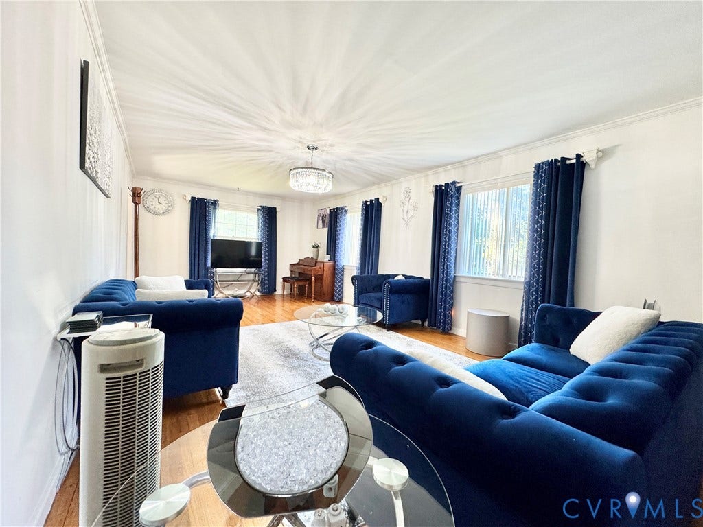 Spacious living area featuring hardwood flooring, crown molding, and a prominent chandelier