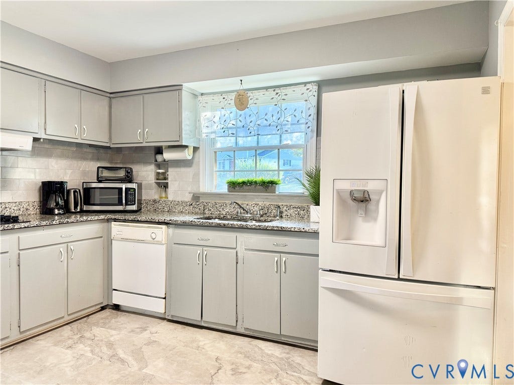 Kitchen featuring light gray cabinetry, speckled countertops, a tile backsplash, and a window