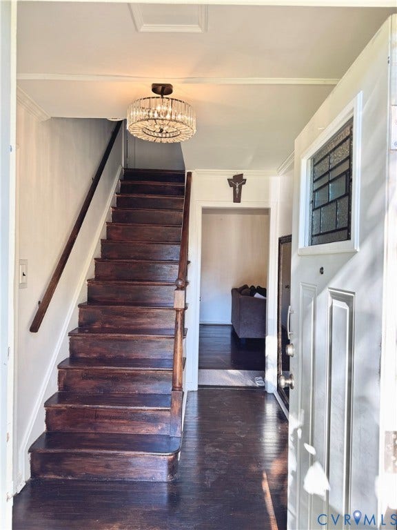 Dark-toned wood staircase with coordinating handrail, crystal chandelier, and front door with decorative glass panel