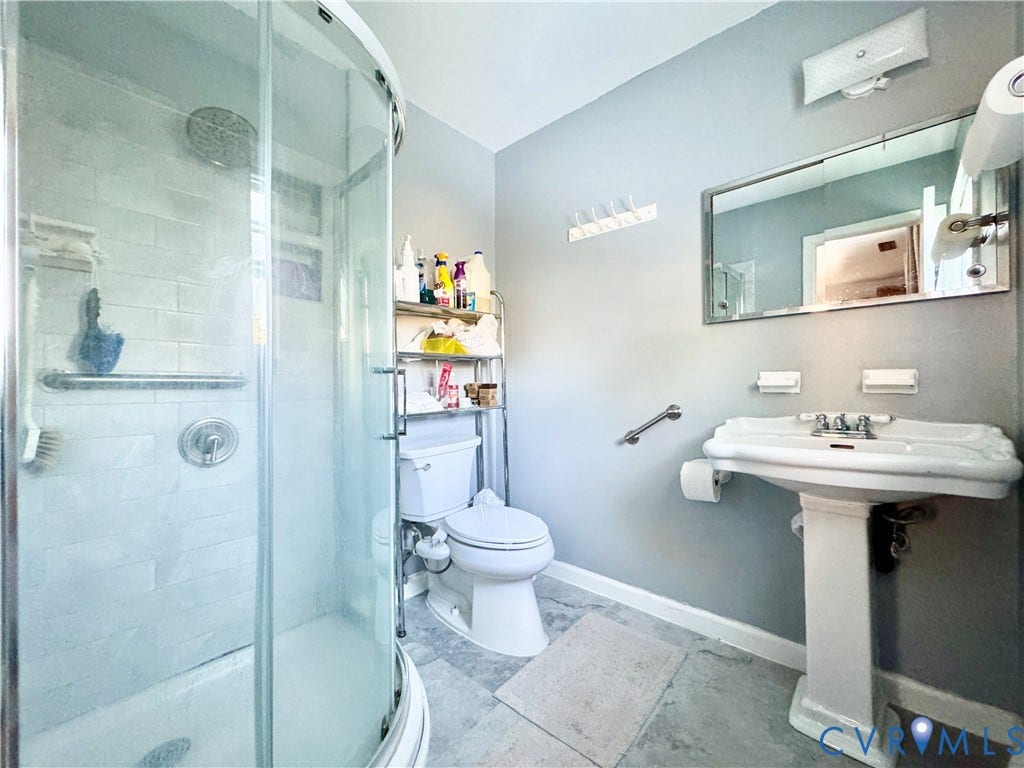 Curved glass shower enclosure, white subway tile shower surround, pedestal sink with chrome fixtures, wall-mounted mirror, and gray wall paint