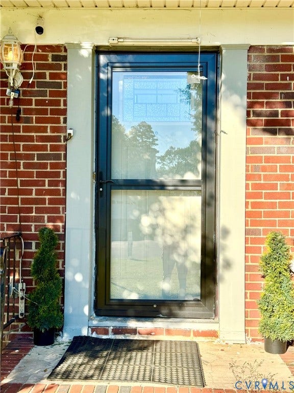 Red brick exterior with a black-framed storm door featuring an upper decorative glass panel, and an exterior wall lantern