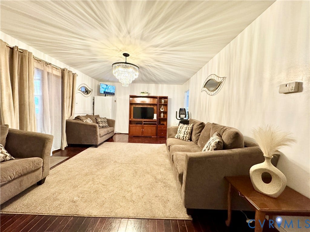 Rich wood-finish flooring with an area rug, a built-in media console, and a central chandelier