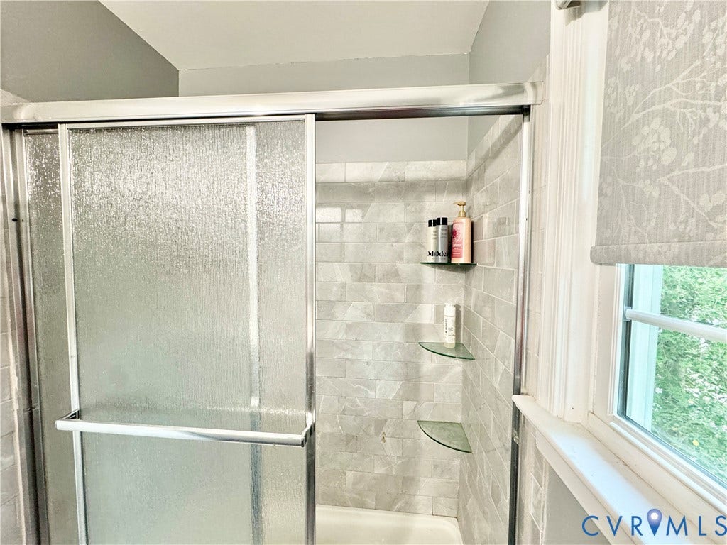 Shower with textured sliding glass doors, tiled walls, and built-in glass corner shelves