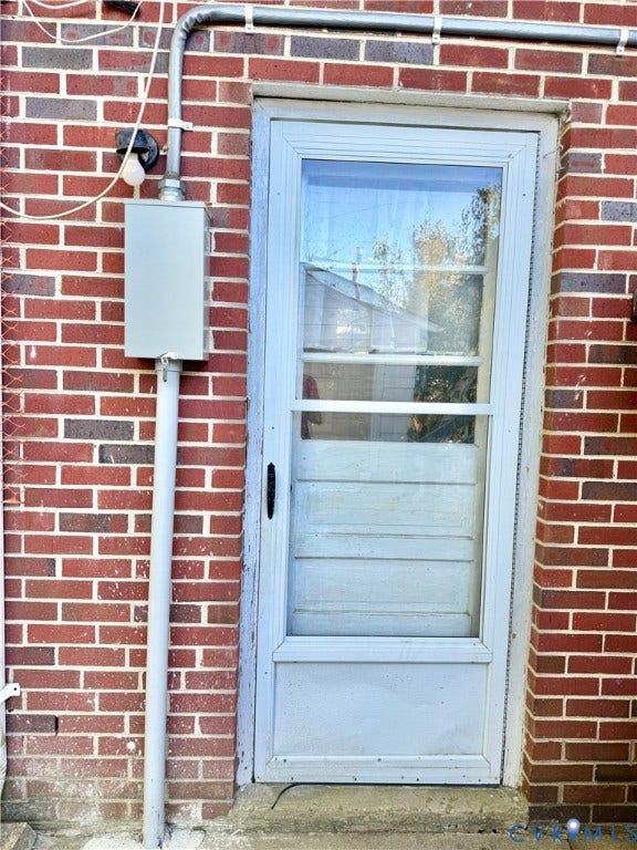 Red brick exterior with a light-colored storm door and an electrical conduit