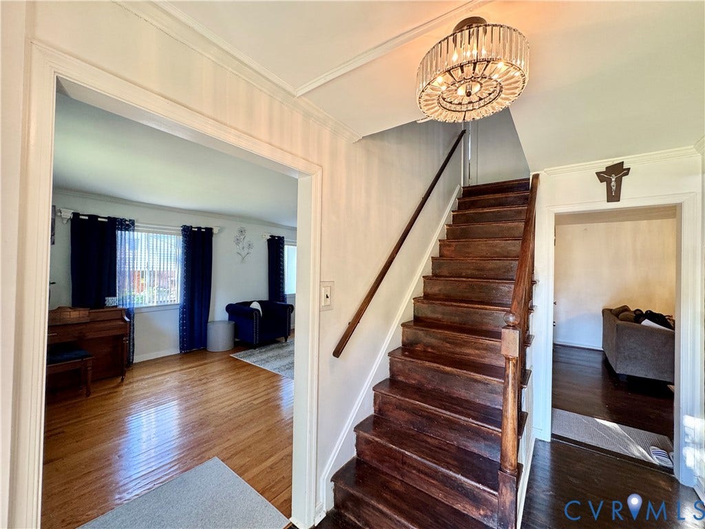Hardwood staircase with a decorative banister, overhead crystal chandelier, and light wood-finish flooring