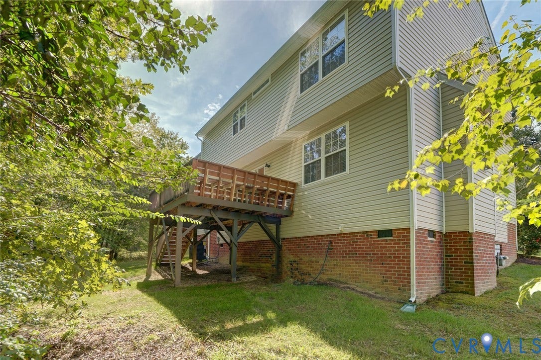 Multi-level exterior featuring light-colored siding, a red brick foundation, and a raised wood deck with railing