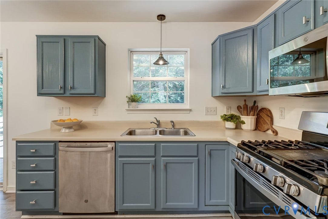 Renovated kitchen featuring custom cabinetry in soft blue-gray finish, stainless steel gas range with multiple burners, undermount sink with brushed nickel hardware, quartz countertops, and a pendant light fixture centered above the work zone