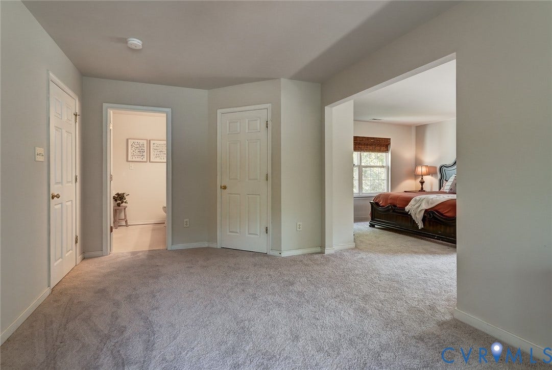 Carpeted room with a doorway leading to a bathroom featuring wood-finish flooring, and a separate doorway to an additional room