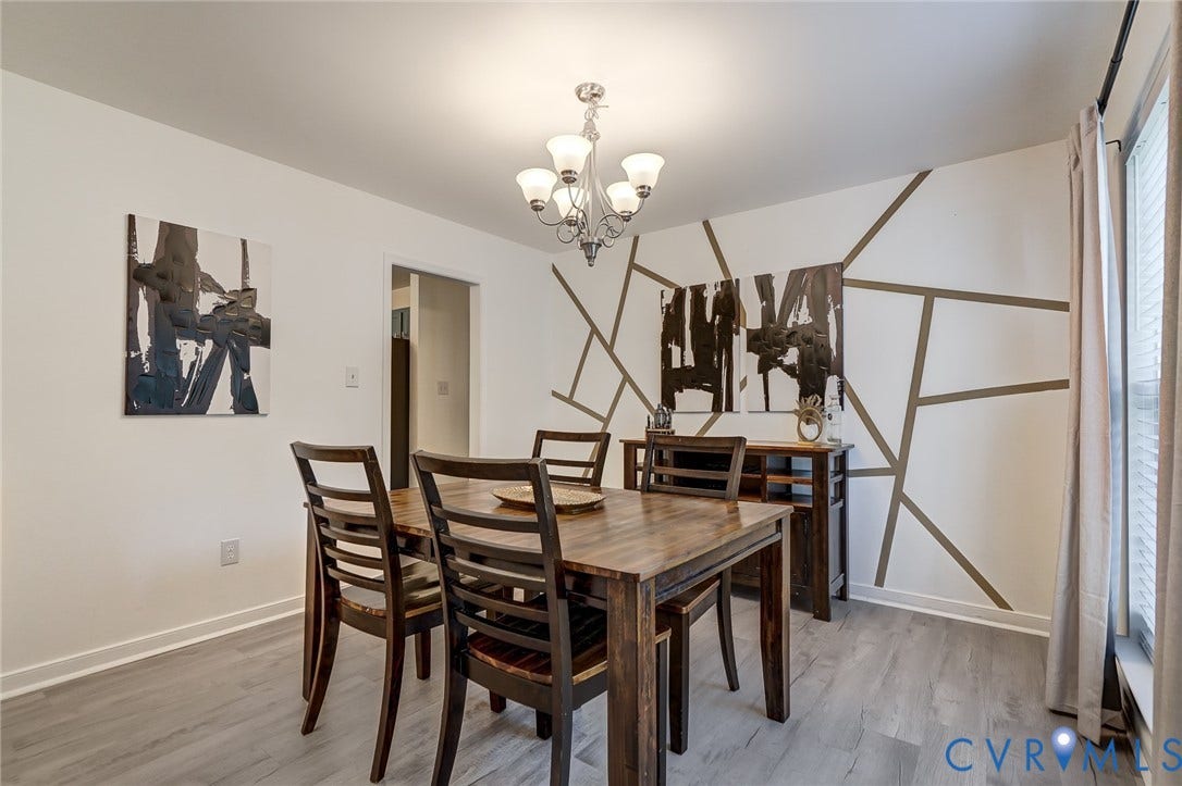 Dining area featuring wood-finish flooring, a contemporary chandelier, and a decorative accent wall
