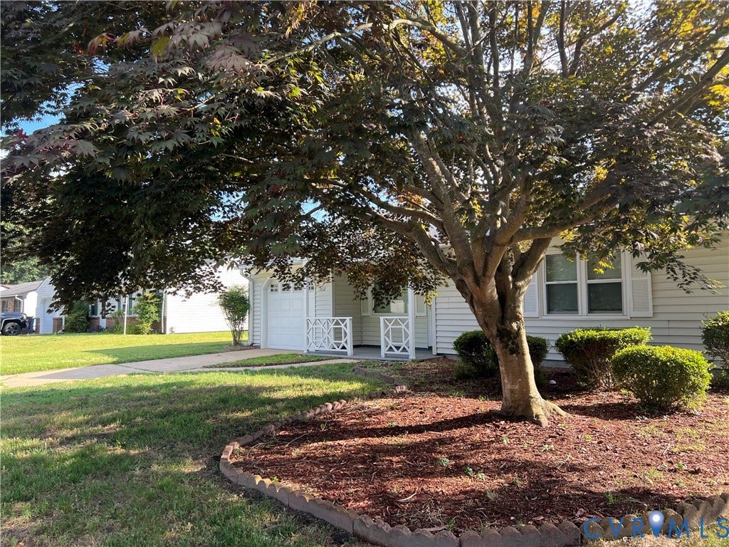 2112 Paramont Avenue, Collegue Park, Chesapeake, VA 23320 White siding exterior with a prominent mature tree, landscaped bed with mulch and decorative edging, an attached garage with a panel door, and a concrete driveway