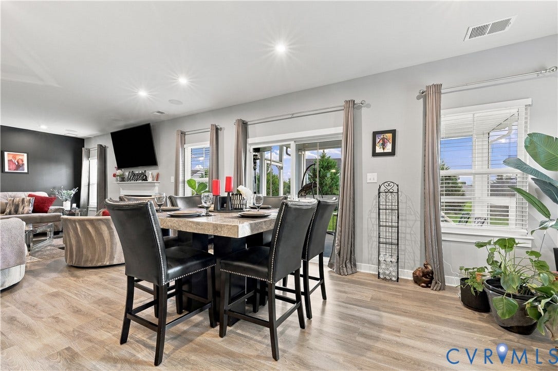 Recessed lighting illuminates the open-concept room featuring wood-finish flooring, multiple windows with blinds, and a sliding glass door
