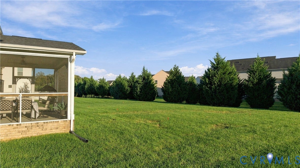 Expansive green lawn with a row of mature evergreen trees, featuring a screened porch with brick base and a shingle roof