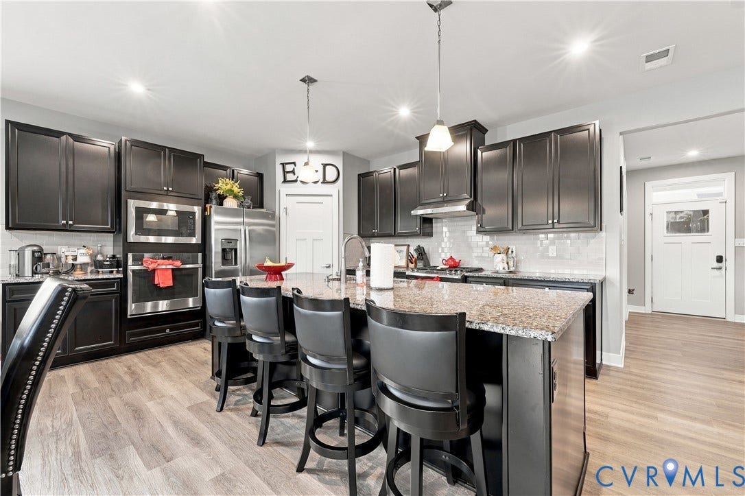 Kitchen featuring dark wood cabinetry, stainless steel appliances, a large island with a stone countertop, and wood-finish flooring
