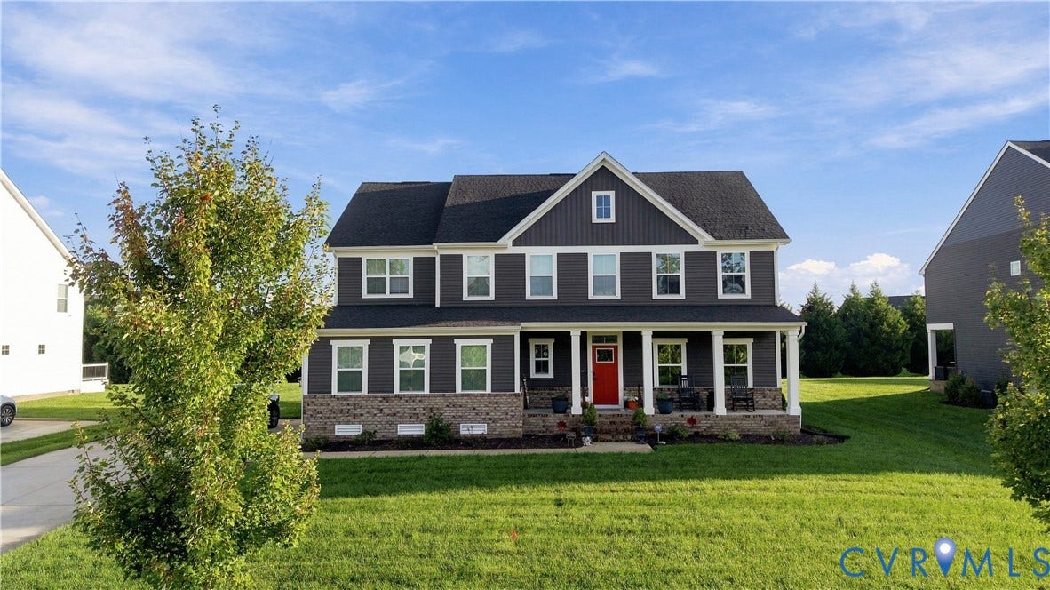 Two-story residence featuring dark siding, a covered front porch, a bright red entry door, white trim, and a dark shingle roof