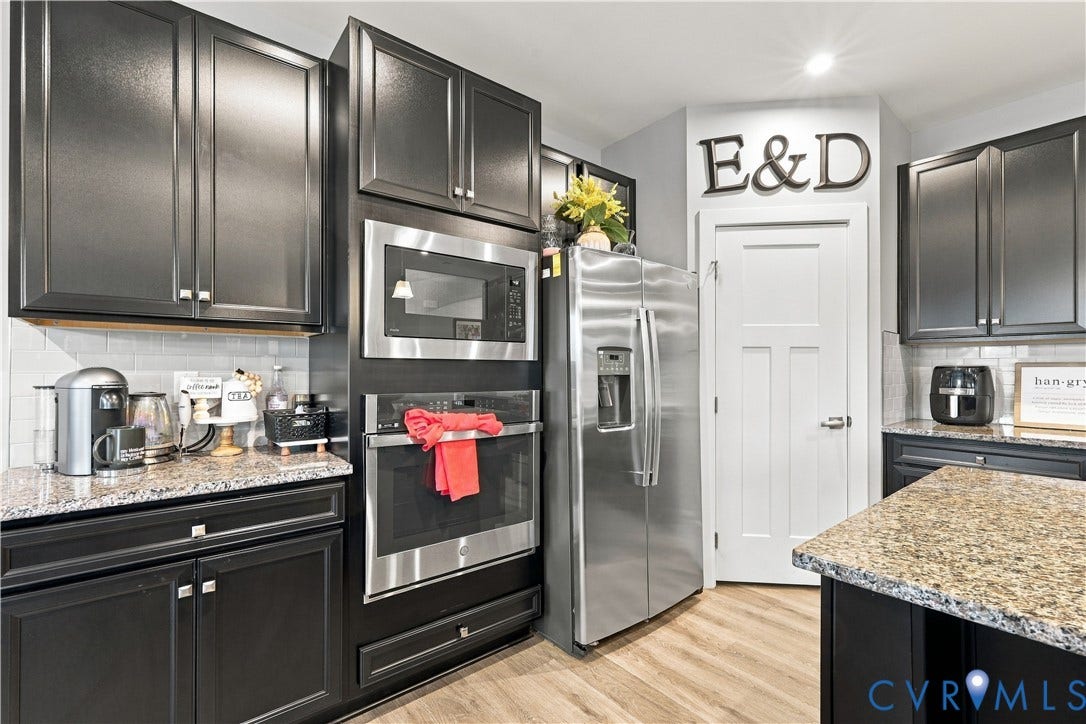 Black cabinetry with silver hardware, granite countertops, stainless steel refrigerator, stainless steel built-in microwave, and stainless steel built-in oven