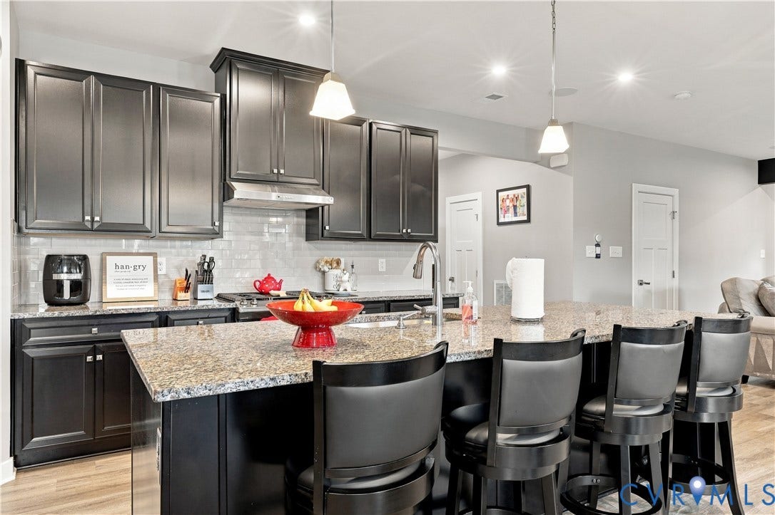 Kitchen featuring dark cabinetry, a subway tile backsplash, a large island with seating, a stainless steel range hood, and pendant lighting