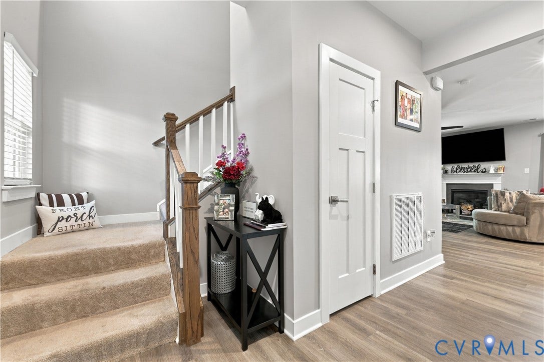 Carpeted staircase with wood railing, wood-finish flooring, white panel door, and a built-in fireplace with mantel