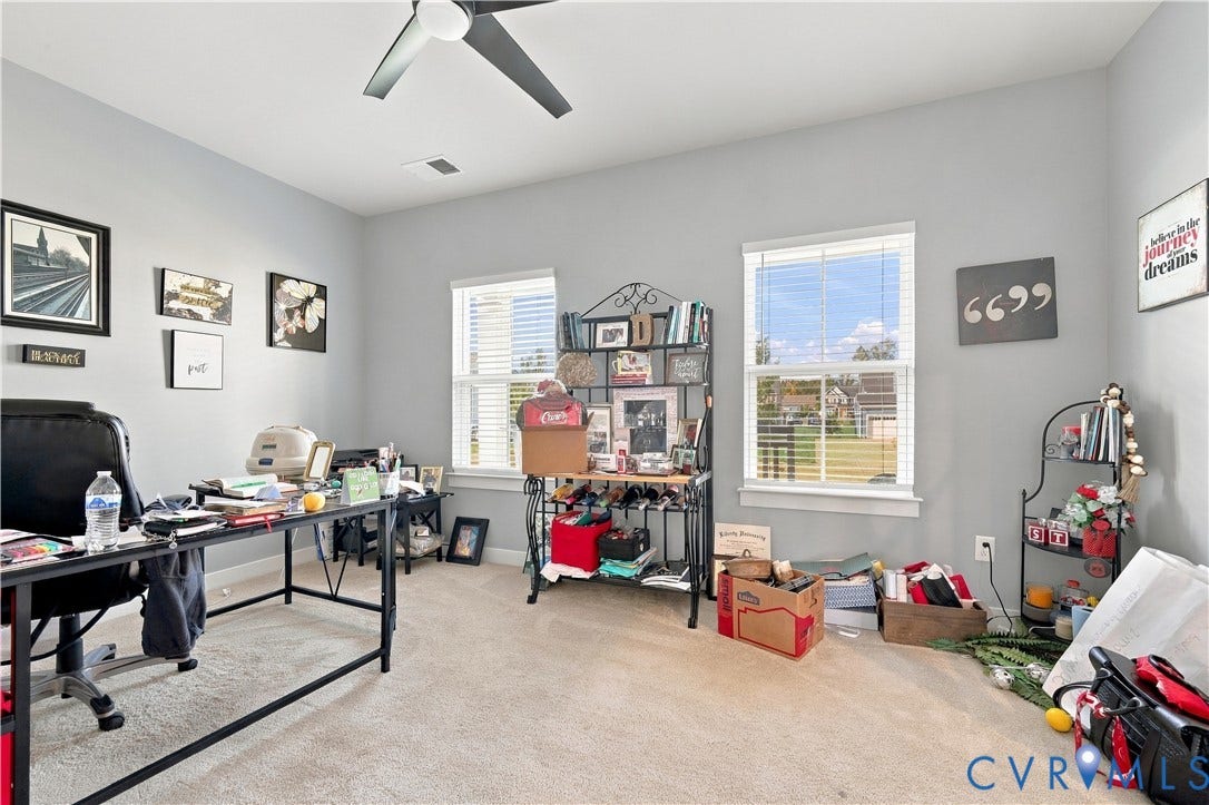 Neutral-toned walls, two distinct windows with blinds, and a ceiling fan with dark blades