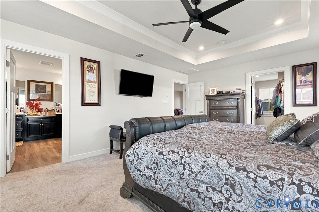 Recessed lighting illuminates the tray ceiling with a black ceiling fan