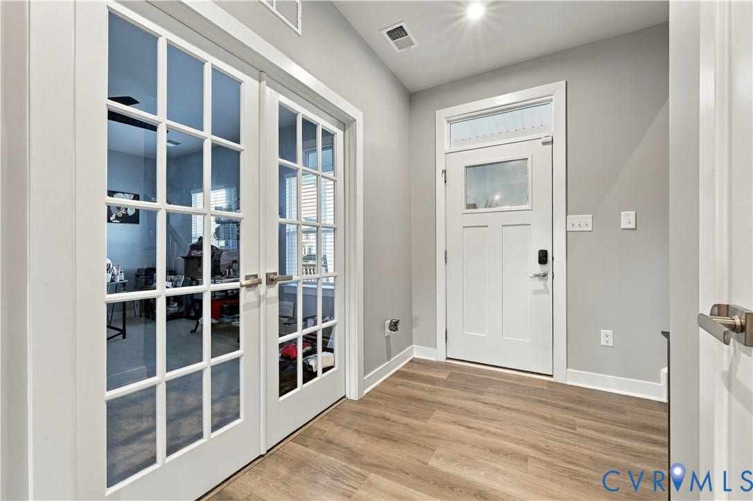 Entryway featuring wood-finish flooring, white paneled door with transom window, and French doors with grid-patterned glass