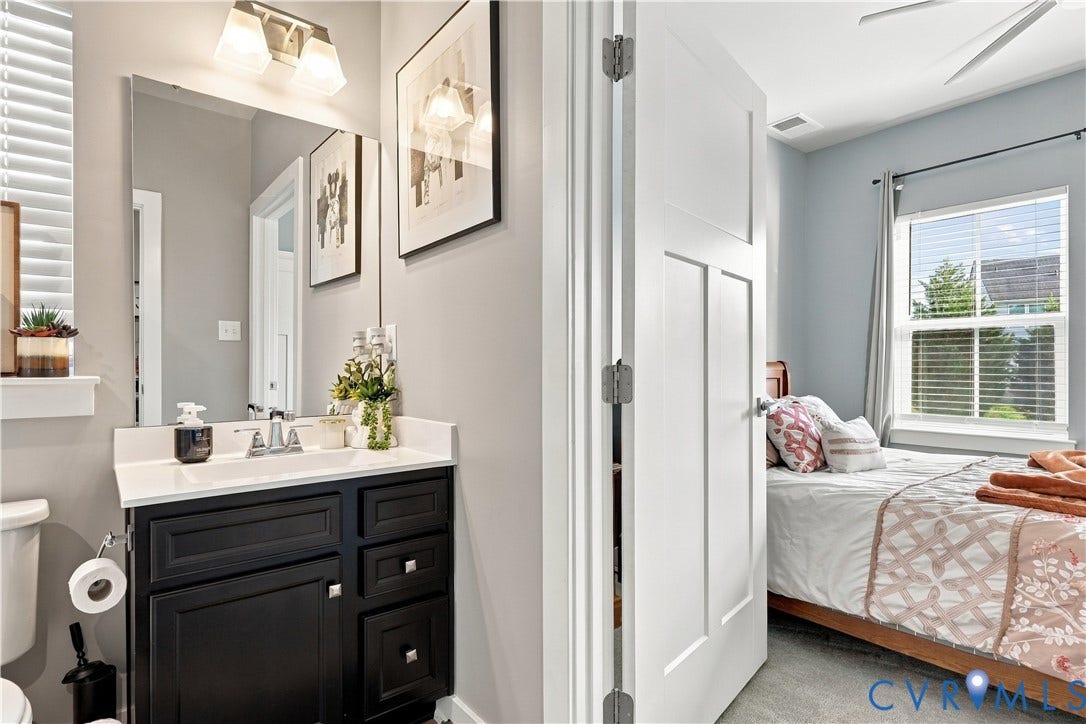 White vanity with a rectangular sink, wall-mounted light fixture, and framed mirror