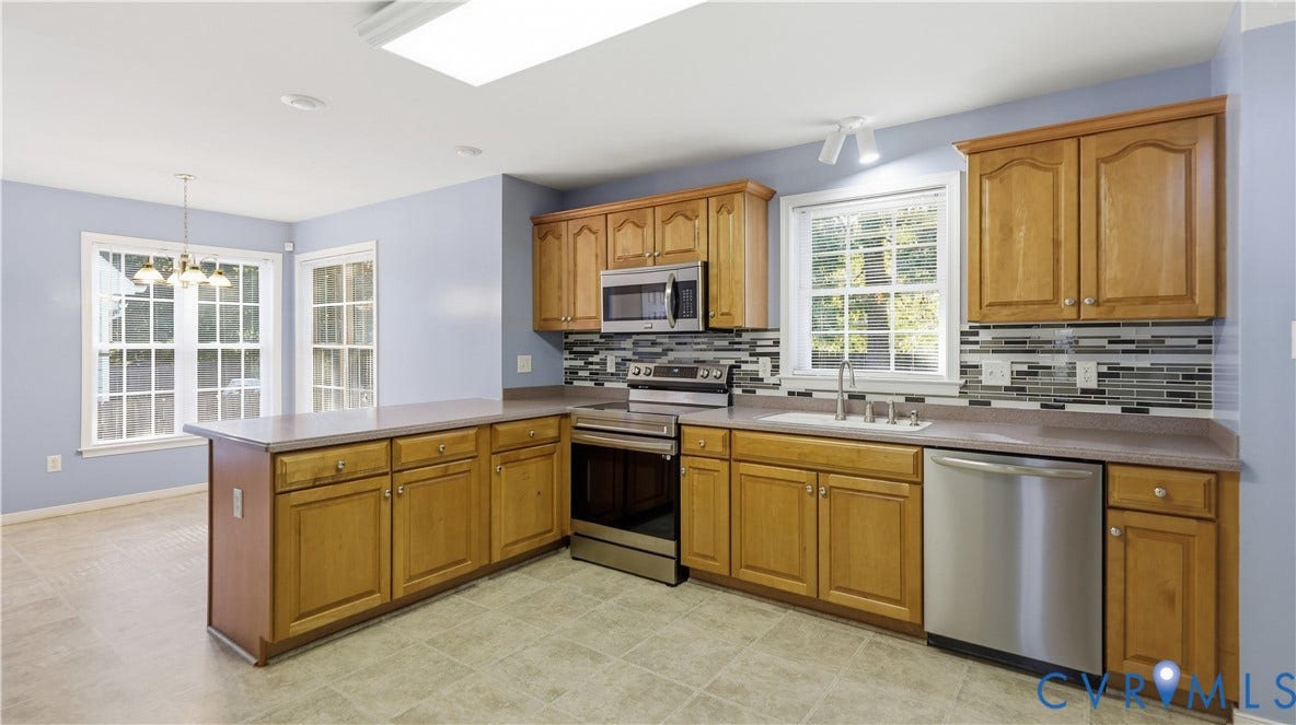 Kitchen featuring wood cabinetry, stainless steel appliances, a tile backsplash, and a skylight