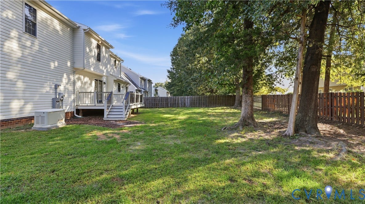 Expansive backyard featuring a manicured lawn, wood privacy fencing, mature trees, and a ground-level deck with steps