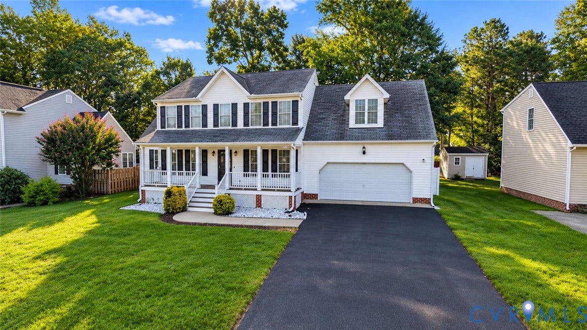 Colonial-style residence featuring a prominent front porch, dormer window, attached two-car garage, and a detached shed