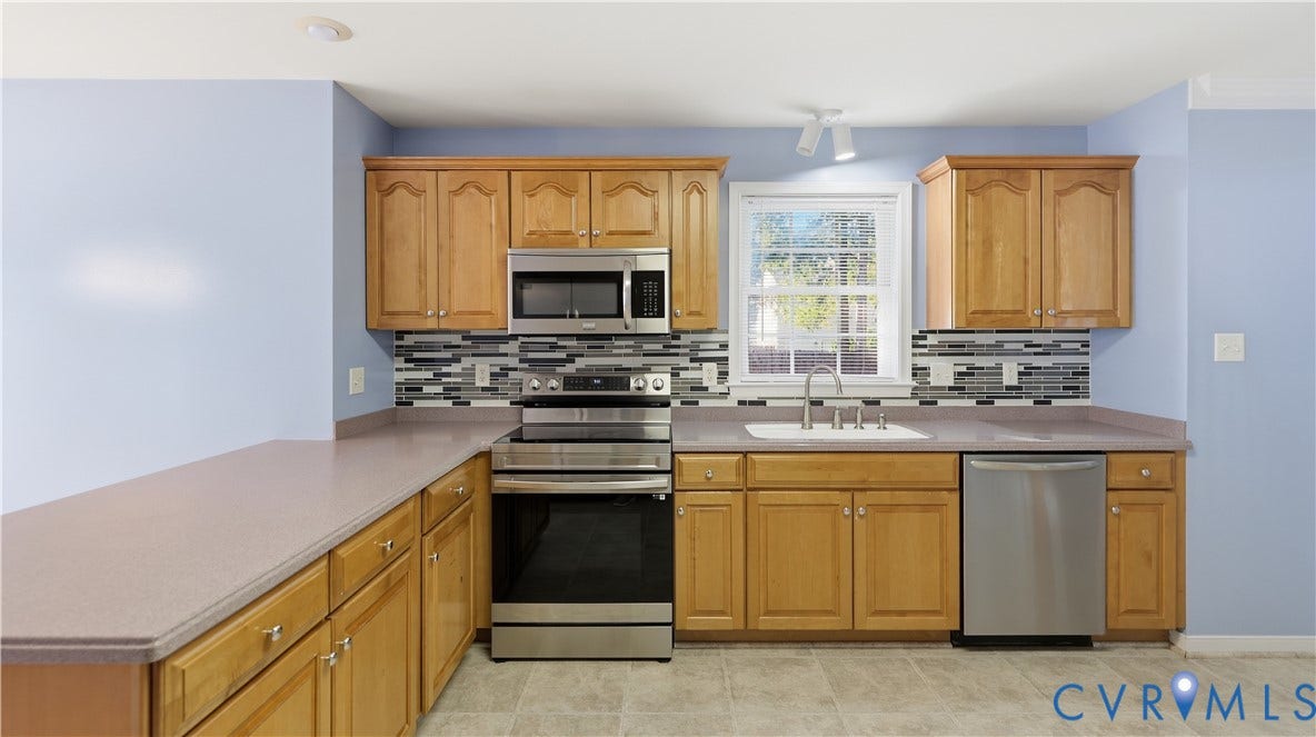 Kitchen featuring wood cabinetry, stainless steel appliances, a tile backsplash, and a window above the sink