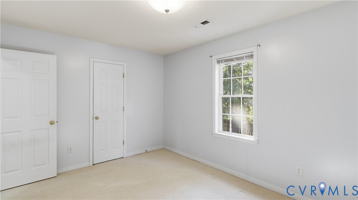 Neutral wall color, carpet flooring, and a single window with white trim