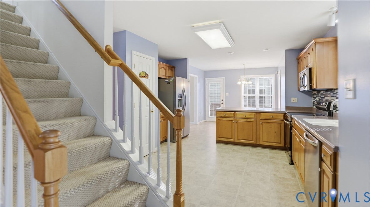 Carpeted staircase with wood handrails, kitchen with wood cabinetry, stainless steel appliances, and tile flooring