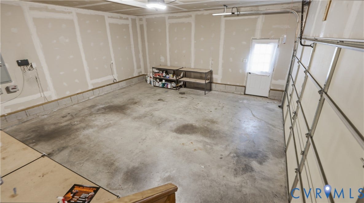 Spacious garage with concrete flooring, exposed drywall, and a side access door