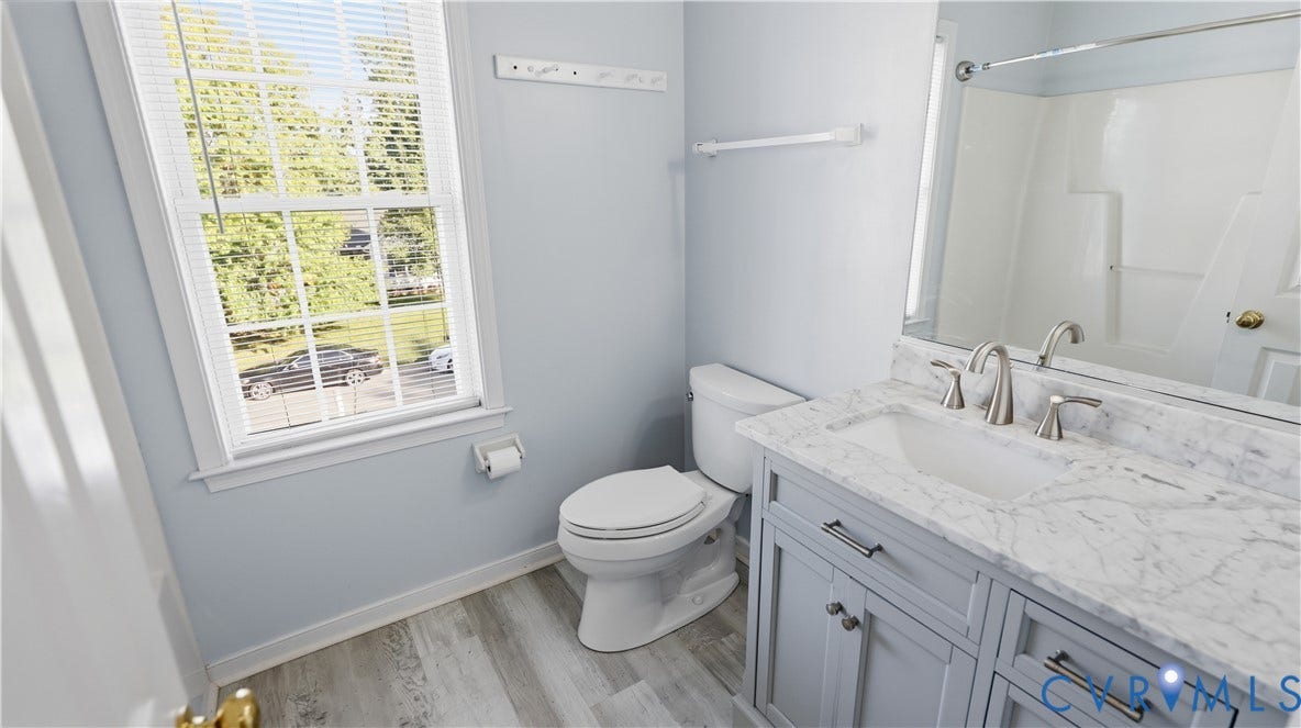 Single window with blinds, wood-finish flooring, white toilet, vanity with undermount sink and brushed nickel faucet, large mirror
