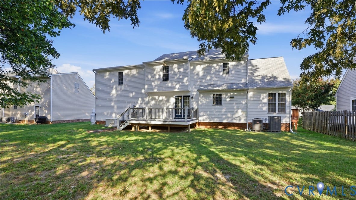 Rear exterior with a wooden deck, white siding, and a spacious grassy area