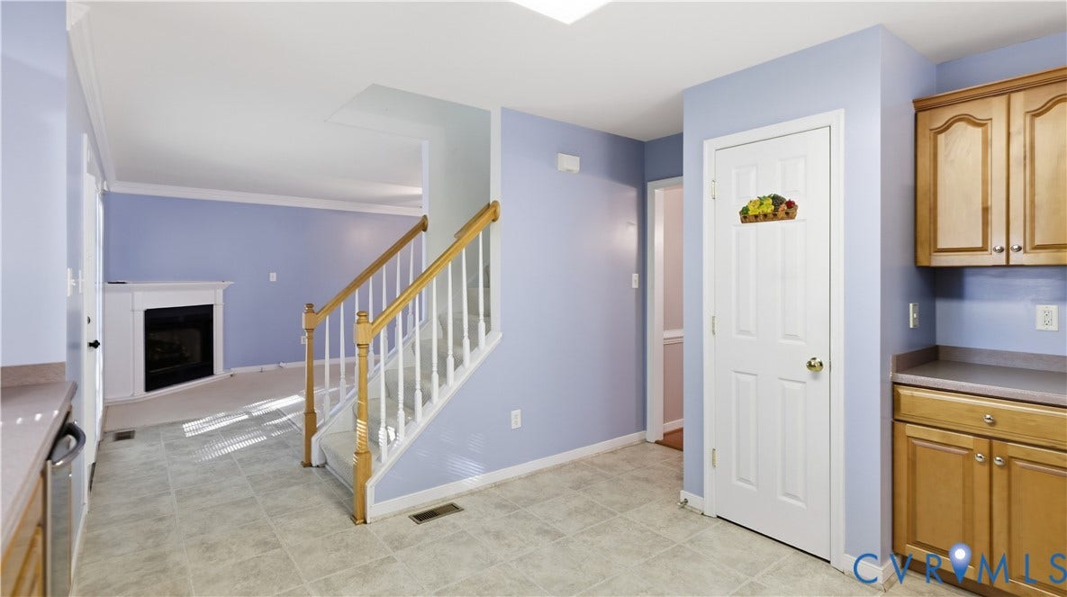 Tiled flooring, wood cabinetry, built-in fireplace, and carpeted stairs with a wood handrail