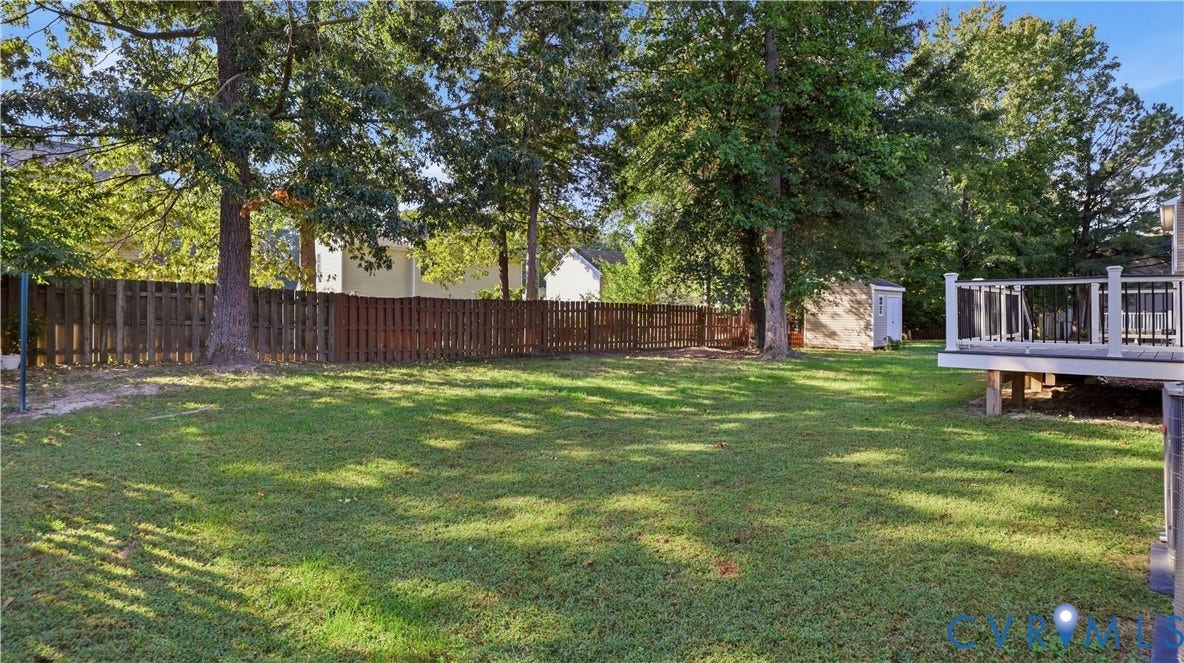 Expansive backyard featuring a manicured lawn, mature trees, privacy fencing, and a built-in deck