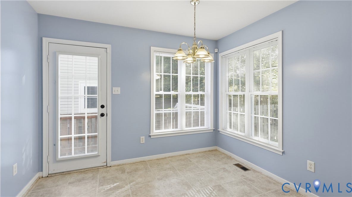 Room featuring tiled flooring, a glass-paned door, two windows with blinds, and a brass-finish ceiling light fixture