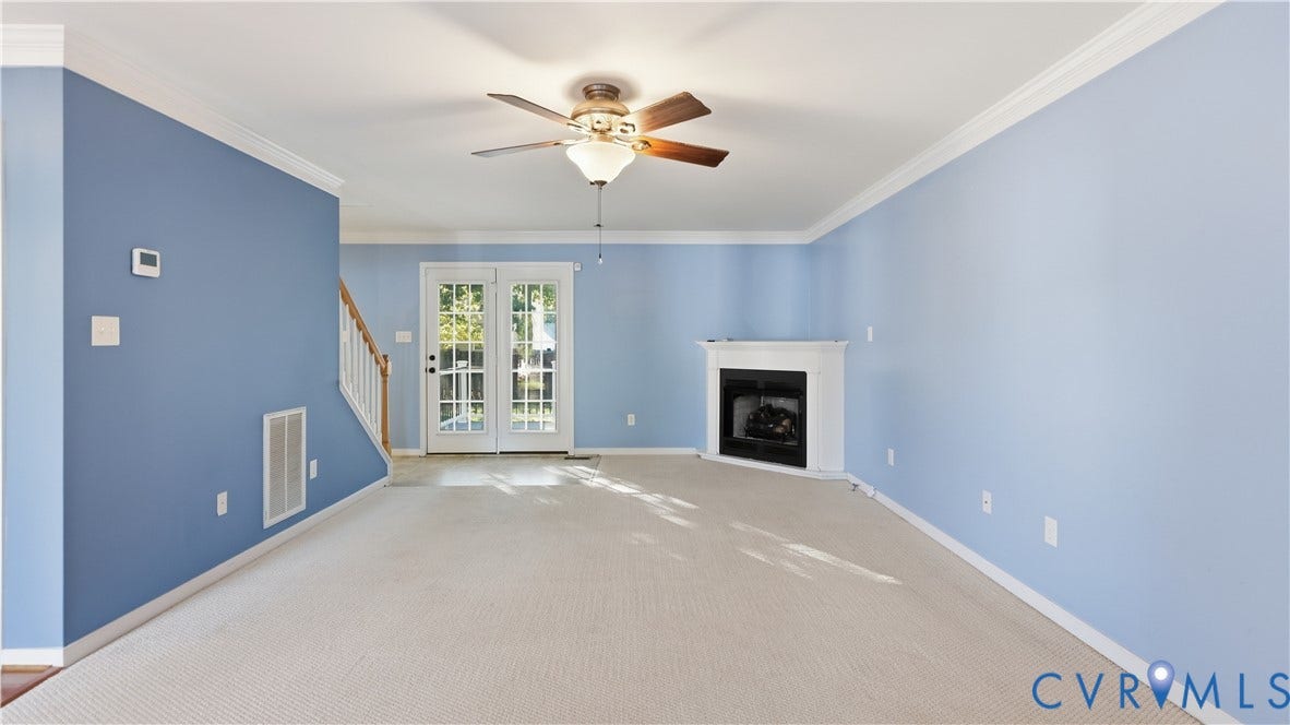 Recessed fireplace with white mantel, ceiling fan with integrated lighting, glass-paneled French doors, light-toned carpeting, and crown molding