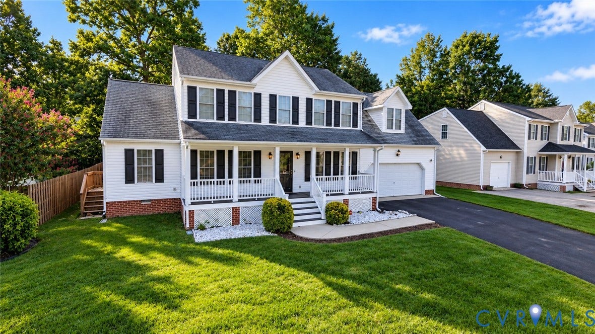 Two-story residence featuring white siding, black shutters, an attached garage, a front porch with white railings, and a paved driveway