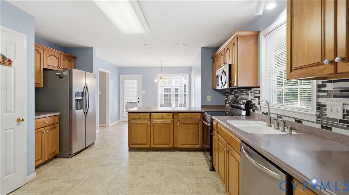 Kitchen featuring wood cabinetry, stainless steel appliances, a multi-tone tile backsplash, and a central island