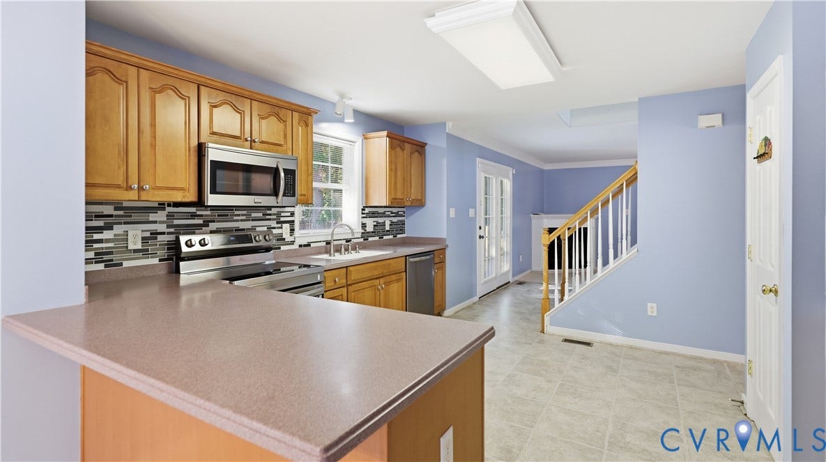 Kitchen featuring wood cabinetry, stainless steel appliances, a multi-tone tile backsplash, and a breakfast bar
