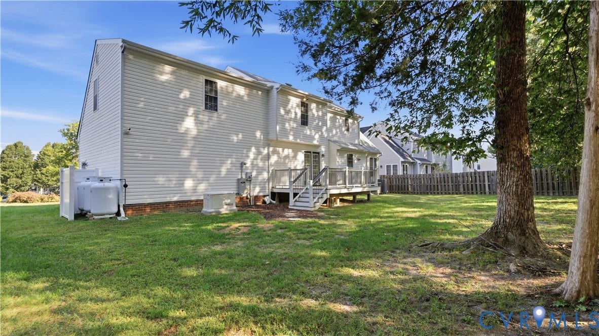 Expansive rear yard with a manicured lawn, mature trees, and a wooden deck