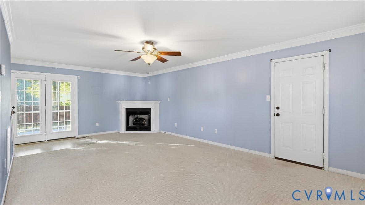 Carpeted living space featuring a ceiling fan with integrated lighting, a corner fireplace with a white mantel, and double paneled glass doors