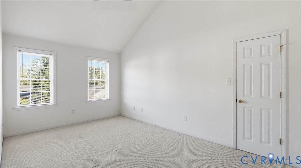 Vaulted ceiling, two double-hung windows, neutral-toned wall-to-wall carpeting, and a six-panel interior door