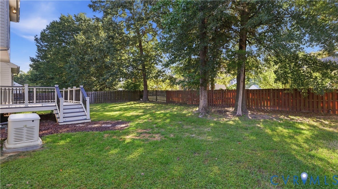 Expansive green lawn with a composite deck, dark wood fencing, and mature trees
