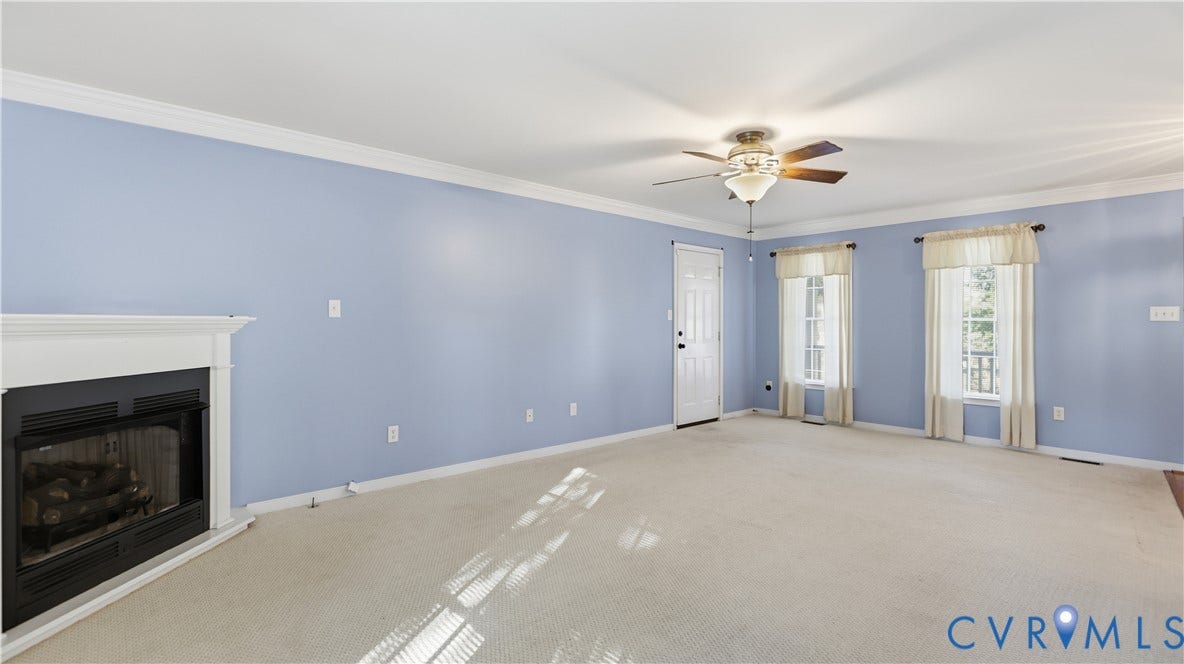 Crown molding, a fireplace, a ceiling fan with integrated lighting, and two windows